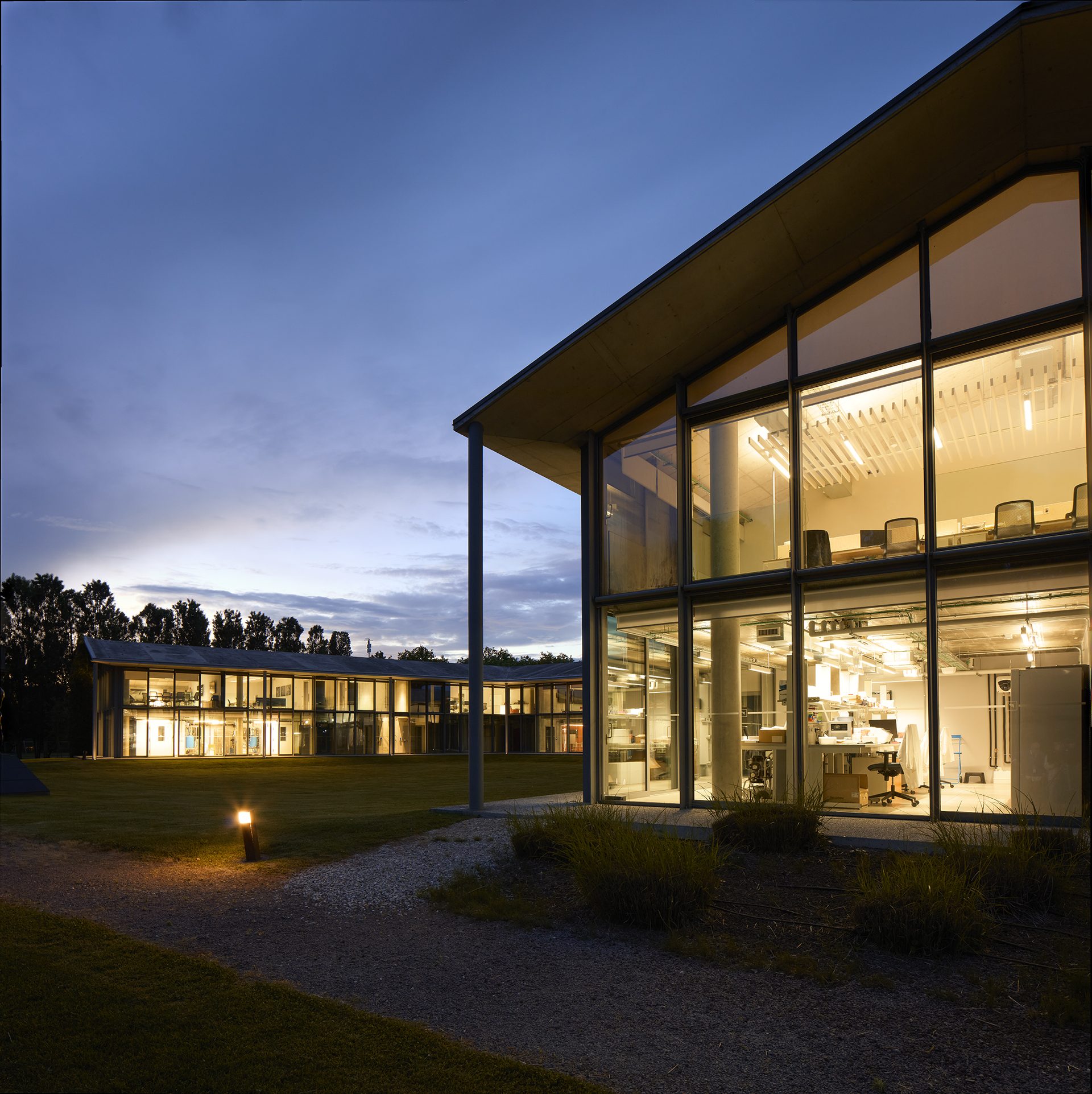 The FFI Roncade campus at dusk, its glass laboratories lit from within.