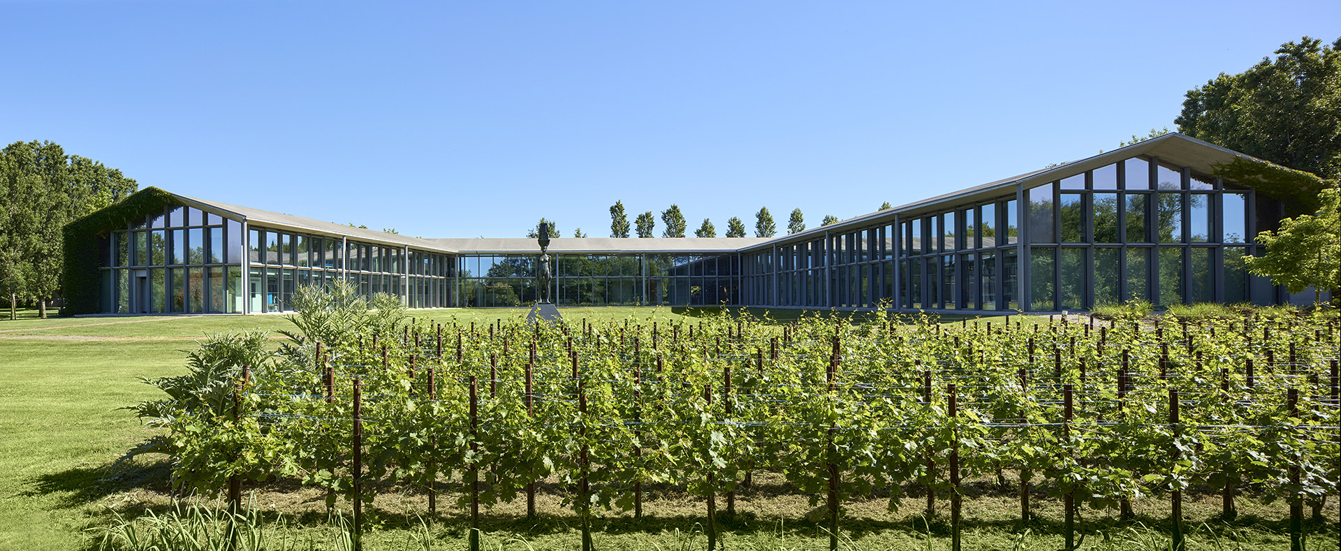 The Roncade campus in daylight, a sculpture on the lawn under a clear sky.